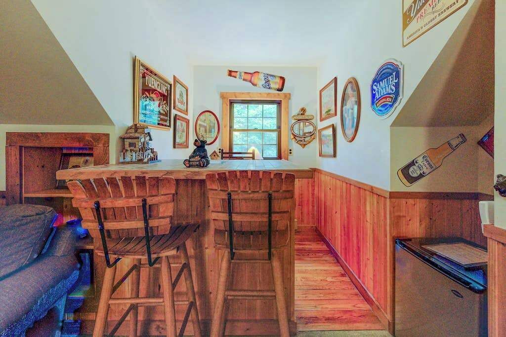 Une cuisine avec des tabourets de bar en bois, un comptoir en bois et divers éléments de décoration murale, notamment des tableaux encadrés et une bouteille de bière.