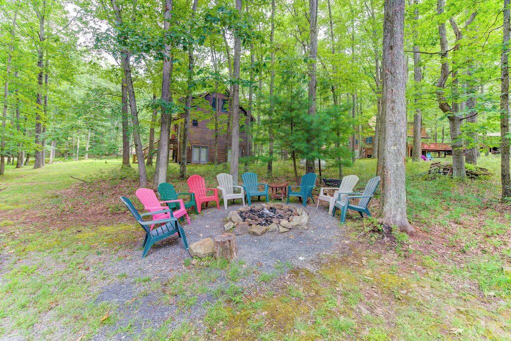 Une cabane entourée d’une forêt, avec un foyer et des fauteuils Adirondack aux couleurs vives.