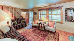 A living room with a staircase, a patterned rug, and a window with blinds.