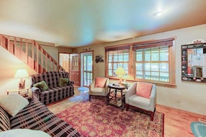 A living room with a staircase, a patterned rug, and a window with blinds.