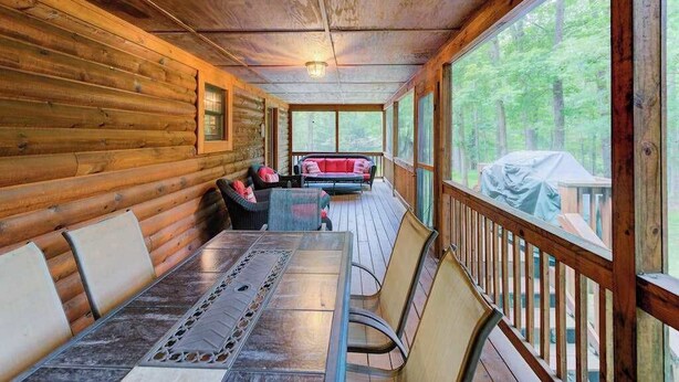 A wooden cabin with a covered porch, a dining table, and a sofa.
