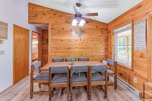 Un interior de madera con una mesa de comedor y sillas, un ventilador de techo y una ventana con vistas.