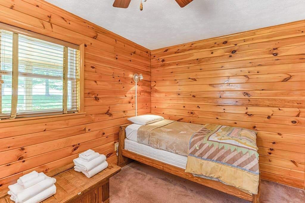 A wooden cabin room with a bed, a nightstand, a lamp, and a window.