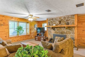 A log cabin interior with a stone fireplace, wooden walls, a ceiling fan, and a television. - Charming 3BR Cabin - MOUNTAIN VIEW - McHenry (McHenry)