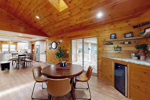 Een houten interieur met een ronde eettafel, stoelen, een koelkast, een wastafel en een open haard.