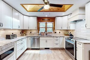 Een moderne keuken met witte kasten, een houten plafond, een inbouwoven en een raam met uitzicht.