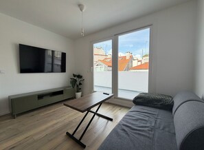 Una sala moderna con televisor de pantalla plana, una mesa de madera, un sofá, una planta en maceta y un ventanal corredizo al exterior.