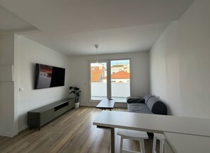 A modern living room with a flat-screen TV, a sofa, a dining table, and a large window. - Apt - Sleeps 4 - Pet Friendly - Central Location (A Coruña)