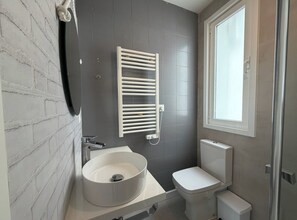 Un baño con lavamanos blanco, inodoro, toallero y ventana.