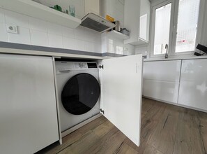 A compact laundry room with a front-loading washing machine, a small shelf with toiletries, and a window with a view. - Apt - Sleeps 4 - Pet Friendly - Central Location (A Coruña)