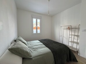 Un dormitorio con cama, almohadas, una ventana, un perchero y una lámpara en el techo.