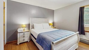 Quarto com cama, mesas de cabeceira e janela com cortinas.