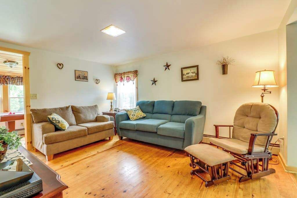 Sala de estar con sofá, sillón, reposapiés, piso de madera y decoración en las paredes.