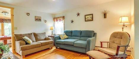 Sala de estar con sofá, sillón, reposapiés, piso de madera y decoración en las paredes.