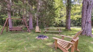 Ein bewaldetes Gebiet mit Schaukel, Picknicktisch und Adirondack-Stühlen.