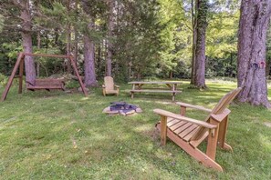 Uma área arborizada com balanço, mesa para piquenique e cadeiras Adirondack.