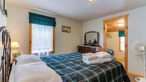 Ein Schlafzimmer mit einem Bett, einem Nachttisch, einem Spiegel, einem Fenster mit Vorhängen, einer Holztür und einem Wandventilator.