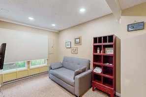 A living room with a grey sofa, a red bookshelf, and a window with blinds. - 2BR - Slope Access - Fireplace (McHenry)