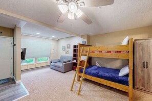 A room with a bunk bed, a sofa, a ceiling fan, a window with blinds, and a door.