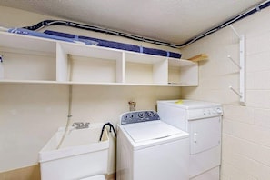 A laundry room with a washing machine, a dryer, and a sink. There are shelves above the washing machine. - 2BR - Slope Access - Fireplace (McHenry)