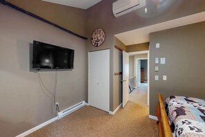 A bedroom with a bed, a television mounted on the wall, a door, and a hallway leading to another room. - 2BR - Slope Access - Fireplace (McHenry)