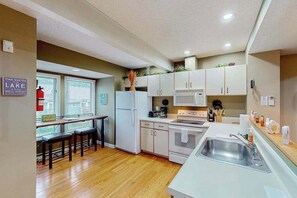A compact kitchen with a refrigerator, microwave, stove, and sink. There are wooden stools at a bar area.