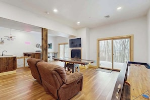 A spacious living area with a sofa, a fireplace, a television, and a large window. - Modern 4BR Cabin - Movie Theater - HOT TUB (McHenry)