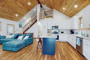 A modern interior with a wooden ceiling, a kitchen with white cabinets, a blue sofa, and a staircase. - Modern 4BR Cabin - Movie Theater - HOT TUB (McHenry)