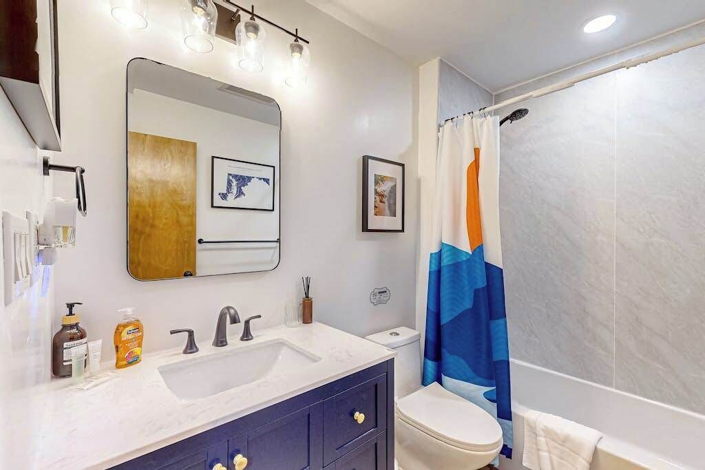 Un baño con lavamanos blanco, armarios azul oscuro, inodoro blanco y cortina de ducha a rayas azules y naranja.