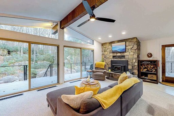 Una sala moderna con chimenea de piedra, ventanas amplias y ventilador de techo.