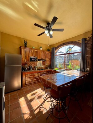 A kitchen with a dining area, a ceiling fan, and a view through a window. - Casa Valentina - Guaju Suite - Just Downtown and Beach (Loreto)