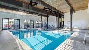Una piscina con interior iluminado por el sol, rodeada de tumbonas y una zona cubierta con techo de madera.