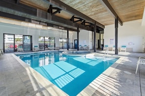 Ein sonnendurchfluteter Pool, umgeben von Liegestühlen und einem überdachten Bereich mit Holzbalkendecke.