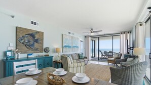 Amplia sala de estar con una mesa de comedor para cuatro personas, un gran mural de peces y un balcón con vista al océano.