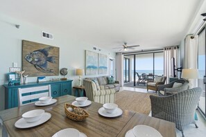 Ein geräumiger Wohnbereich mit Esstisch für vier Personen, einem großen Wandbild mit Fischmotiven und einem Balkon mit Meerblick.