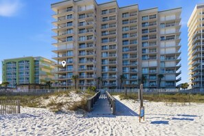 Ein mehrstöckiges Hotel mit Balkonen, ein Sandstrand davor und ein klarer, blauer Himmel.