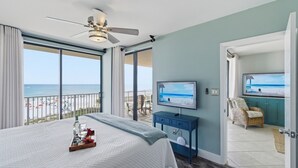 Un dormitorio con cama, televisión, ventilador de techo y balcón con vista a la playa.