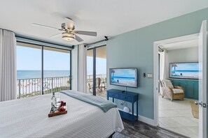 Ein Schlafzimmer mit Bett, Fernseher, Deckenventilator und einem Balkon mit Blick auf den Strand.