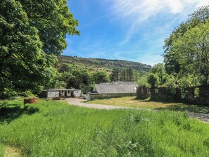A rural setting with a stone building, a grassy field, and a hill in the background. - Daffodil Cottage (Treorchy)