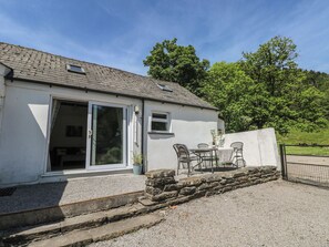 A single-story building with a gravel driveway, a stone wall, and a patio with outdoor furniture. - Daffodil Cottage (Treorchy)