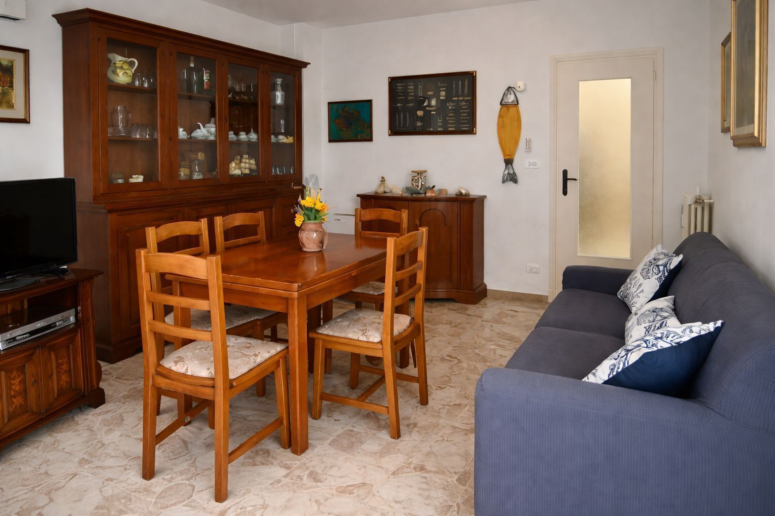 Un soggiorno con tavolo da pranzo in legno, sedie, divano, credenza, televisore e una porta.