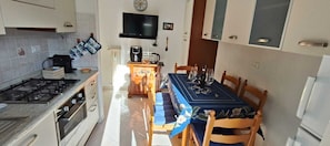 A compact kitchen with a gas stove, oven, and a dining table set for four. - Sanremo Note di Mare: Relax & Comfort Apartment, a 10-meter walk from downtown  (Sanremo)