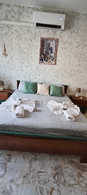 Ett hotellrum med en säng, två sängbord, en luftkonditionering, en tavla och ett marmorgolv.