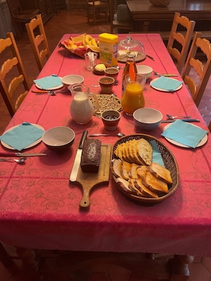 Una mesa de comedor con diversos alimentos para el desayuno, incluyendo pan, mantequilla, mermelada y jugo de naranja.