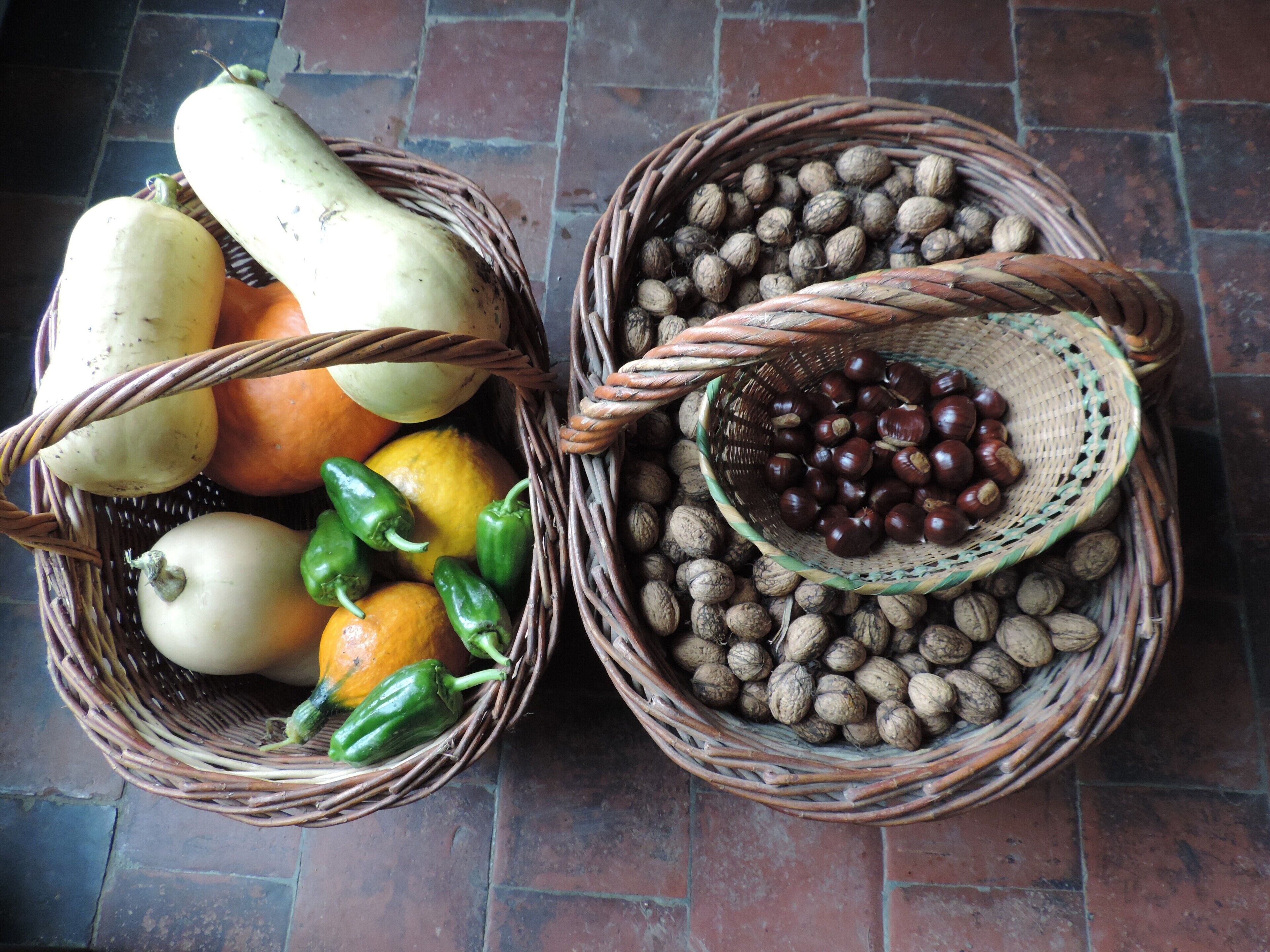 Two wicker baskets filled with various fruits and nuts on a tiled floor.