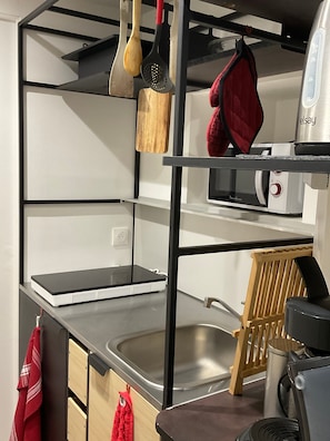 Cocina con microondas incorporado, un lavamanos y utensilios de madera colgando.