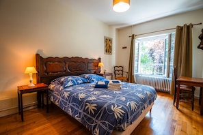 Un dormitorio con una cama grande, dos mesitas de noche, una ventana con cortinas y un radiador.