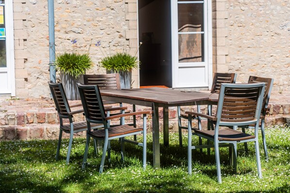 A round table with six chairs, a potted plant, and a stone wall in the background.
