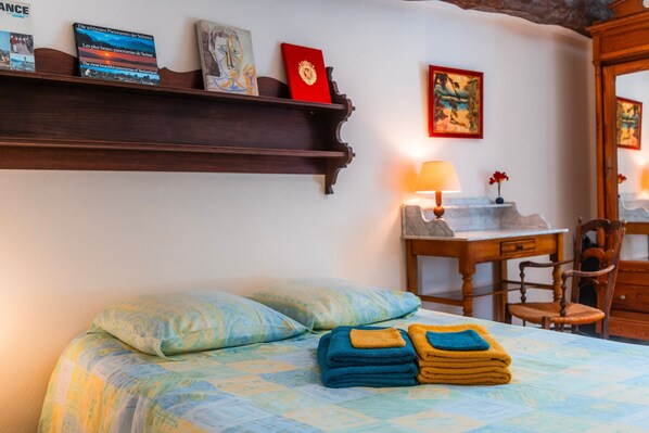 Una habitación de hotel con una cama, un escritorio, una silla y una estantería con libros y un cuadro.