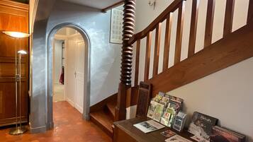 Un escalier avec des balustrades en bois, un luminaire fixé au mur et une étagère où sont exposés des livres et des magazines.